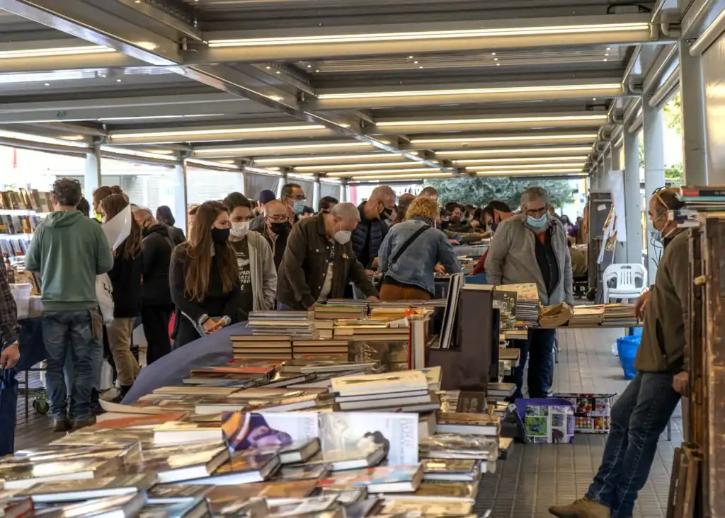 Mercat Sant Antoni Barcelona durante la feria de libros dominical, con mesas repletas de ejemplares y visitantes de todas las edades explorando títulos bajo una estructura cubierta. El ambiente refleja cultura local, comunidad y pasión por la lectura.