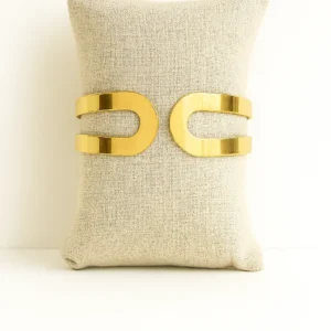 Pulsera acero dorado Iris con diseño curvo moderno sobre cojín beige